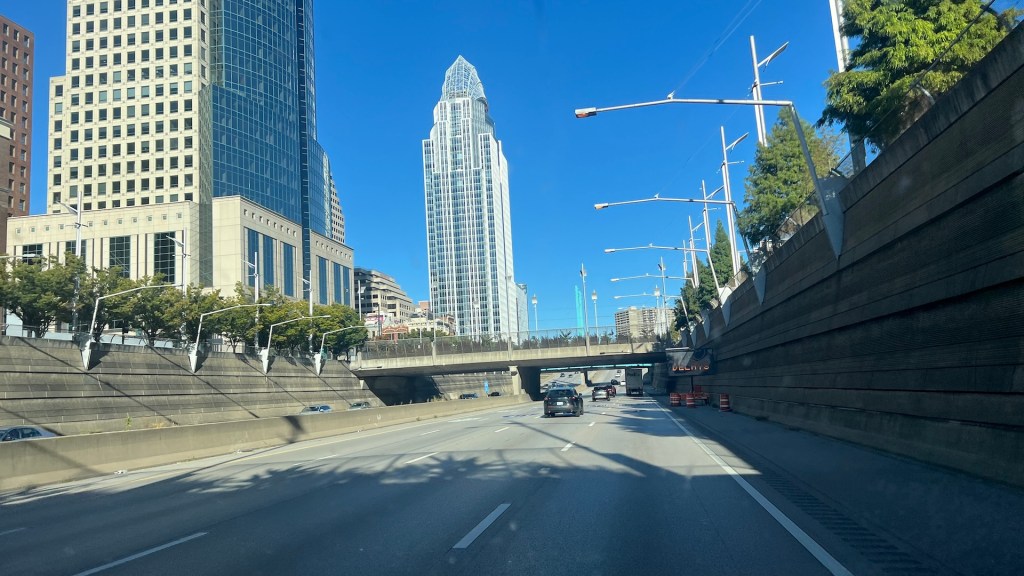 View of a city highway with modern skyscrapers in the background under a clear blue sky.